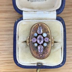 May include: A gold ring with a large oval-shaped setting featuring a cluster of pink and white gemstones. The ring is in a blue velvet ring box with the inscription "Jewellers Bristol Bridge Bristol England".
