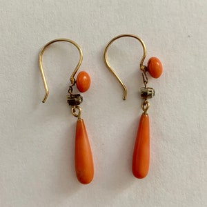 Pu&ograve; includere: Un paio di orecchini pendenti in oro con pietre di corallo a forma di goccia e piccole perle rotonde di corallo.