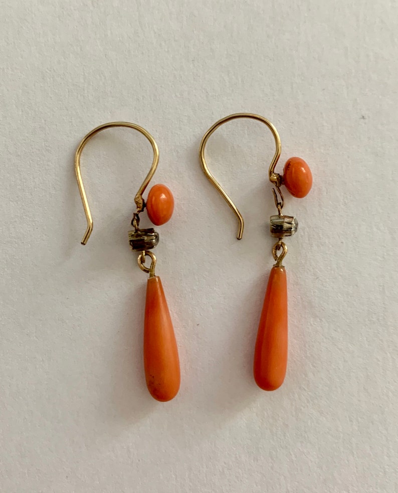 Pu&ograve; includere: Un paio di orecchini pendenti in oro con pietre di corallo a forma di goccia e piccole perle rotonde di corallo.