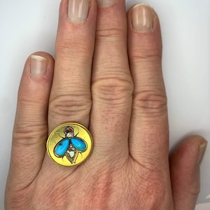 Może przedstawiać: Złoty pierścionek z motywem muchy z turkusowymi i białymi kamieniami.