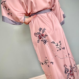 May include: A pink satin robe with a floral print and a gray sash. The robe has long sleeves and a knee-length hem.