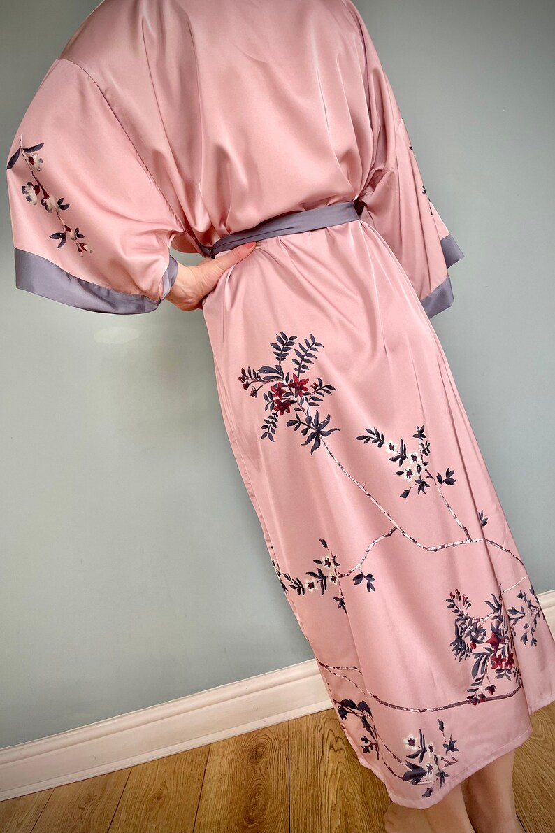 May include: A pink satin robe with a floral print and a gray sash. The robe has long sleeves and a knee-length hem.