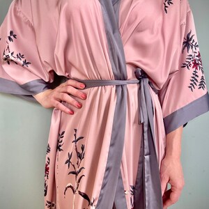 May include: A pink satin robe with a gray trim and floral print. The robe has a tie belt and long sleeves.