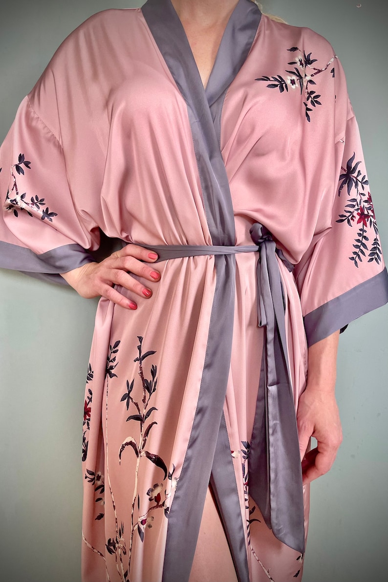 May include: A pink satin robe with a gray trim and floral print. The robe has a tie belt and long sleeves.