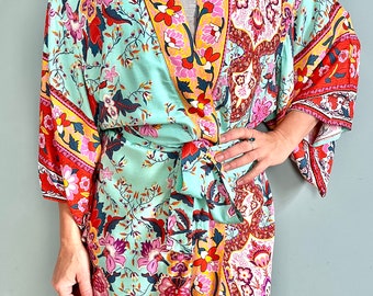 Könnte beinhalten: Eine lange, fließende Robe mit einem Blumendruck in den Farben Rosa, Rot, Gelb und Blau. Die Robe hat einen Bindegürtel in der Taille und lange, fließende Ärmel.