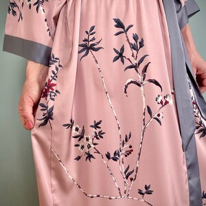 May include: A pink satin robe with a gray sash and floral print. The robe has long sleeves and a tie closure.