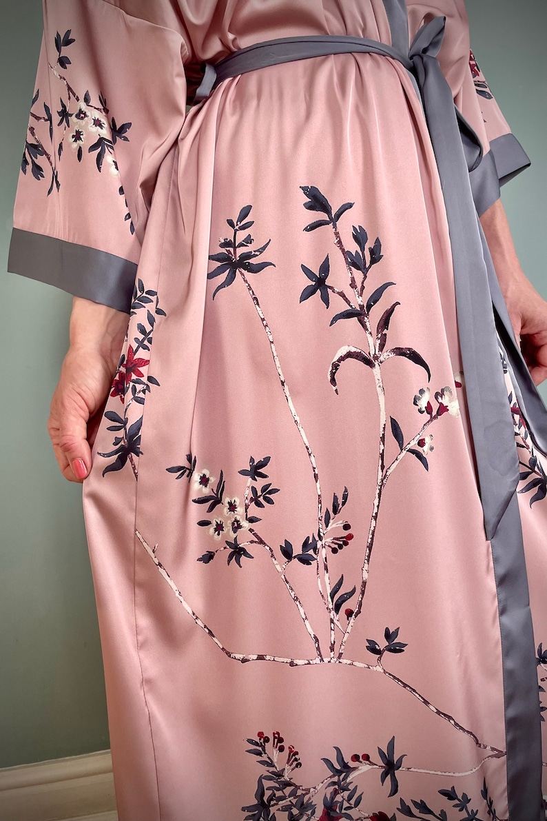 May include: A pink satin robe with a gray sash and floral print. The robe has long sleeves and a tie closure.