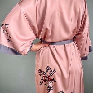May include: A pink satin robe with a floral print and a gray sash. The robe has long sleeves and a relaxed fit.