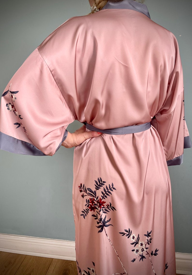 May include: A pink satin robe with a floral print and a gray sash. The robe has long sleeves and a relaxed fit.