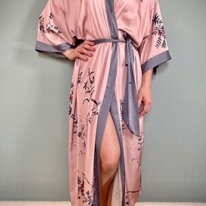 May include: A long, pink satin robe with a floral print and a gray trim. The robe has a tie belt and a front opening.