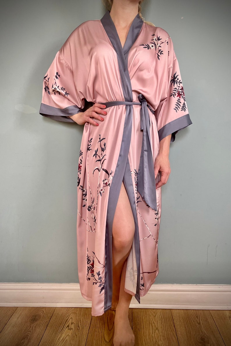 May include: A long, pink satin robe with a floral print and a gray trim. The robe has a tie belt and a front opening.