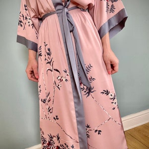 May include: A long, pink satin robe with a floral print and a gray satin sash. The robe has long sleeves and a shawl collar.