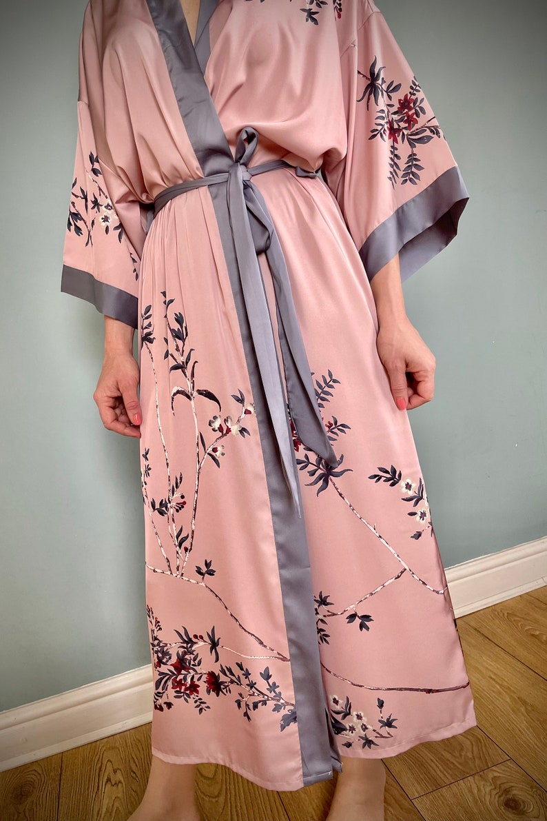 May include: A long, pink satin robe with a floral print and a gray satin sash. The robe has long sleeves and a shawl collar.