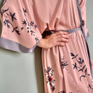 May include: A pink satin robe with a floral print and a gray trim. The robe has a tie belt and long sleeves.