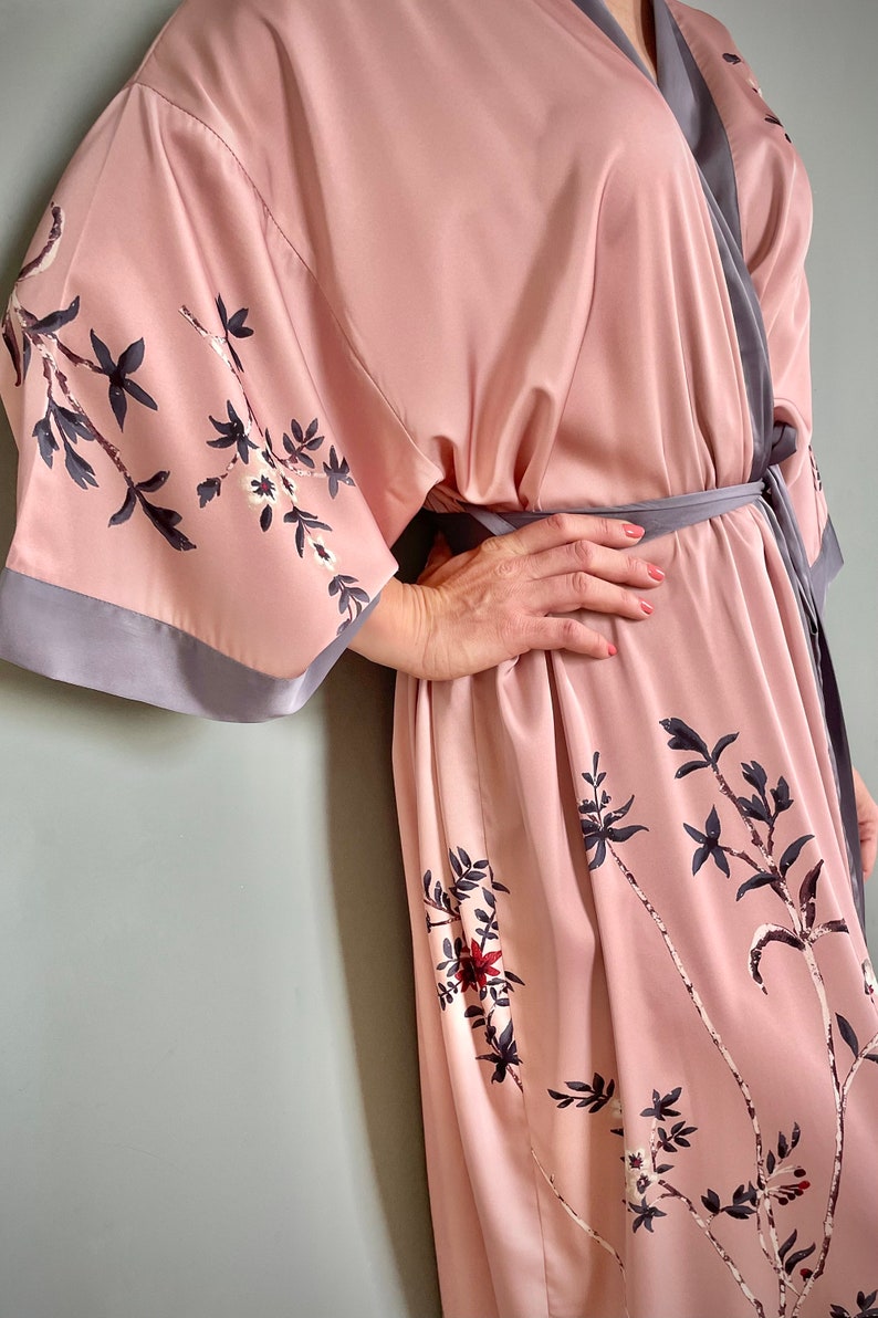 May include: A pink satin robe with a floral print and a gray trim. The robe has a tie belt and long sleeves.