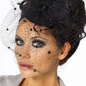 May include: A black veil with a black feather and black polka dots. The veil is worn over a woman's hair and covers her face.