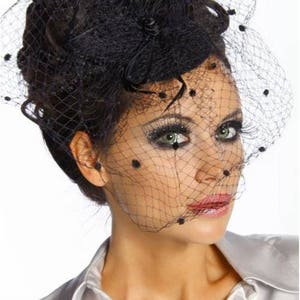 May include: A black veil with small black dots and a black feather accent. The veil is worn over a woman's hair and covers her face.