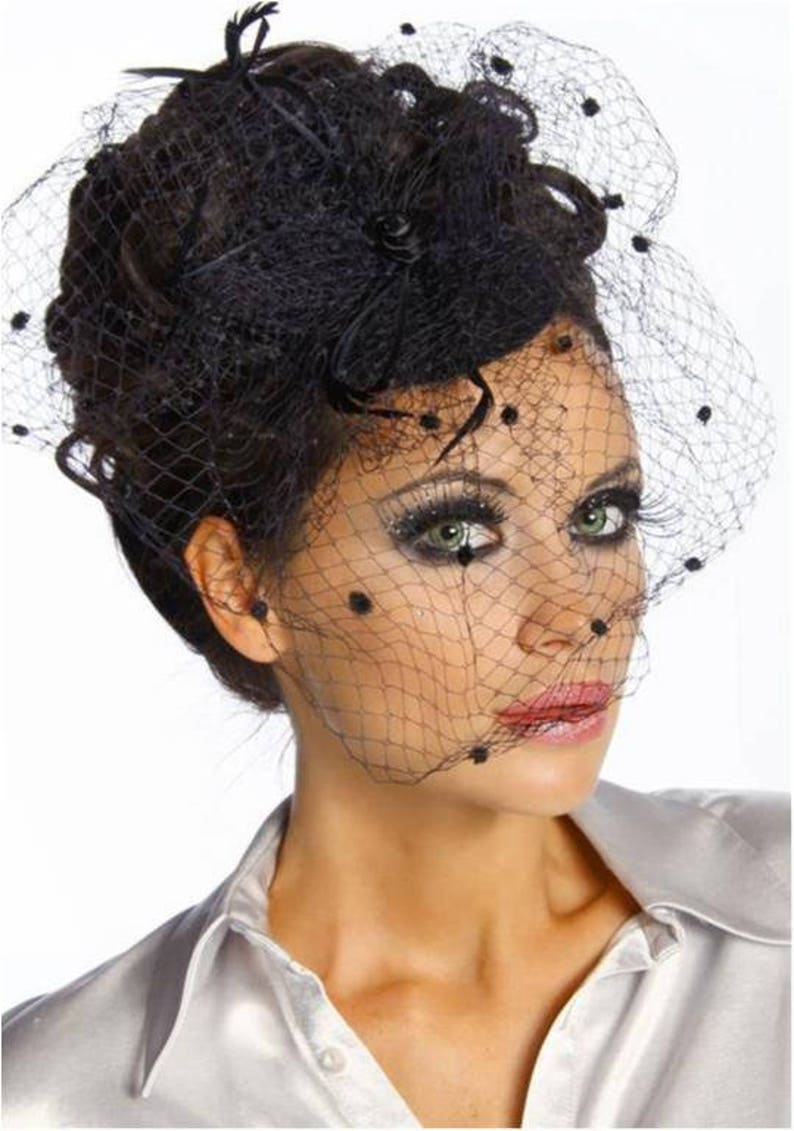 May include: A black veil with small black dots and a black feather accent. The veil is worn over a woman's hair and covers her face.