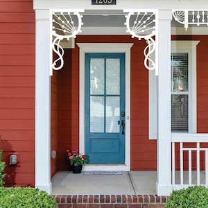 May include: Exterior view of a house with a red facade, white trim, and a teal front door. Decorative white brackets adorn the porch. The house number "1205" is visible above the door. A small flower pot sits near the door.