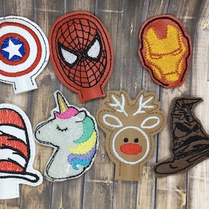 May include: Set of seven embroidered iron-on patches featuring various characters, including a red and blue Captain America shield, a red and black Spiderman mask, a yellow and red Iron Man mask, a red and white Cat in the Hat hat, a rainbow unicorn, a brown reindeer, and a brown Harry Potter Sorting Hat.
