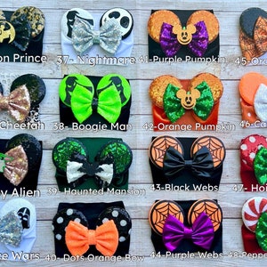 May include: A collection of 10 Halloween-themed headband sets with different character designs, including a lion, cheetah, alien, spiderwebs, pumpkins, and candy corn. Each headband features a pair of mouse ears with a bow.