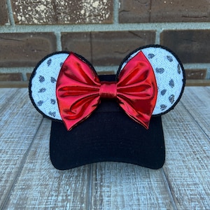 May include: Black baseball cap with red bow and white and black spotted ears.