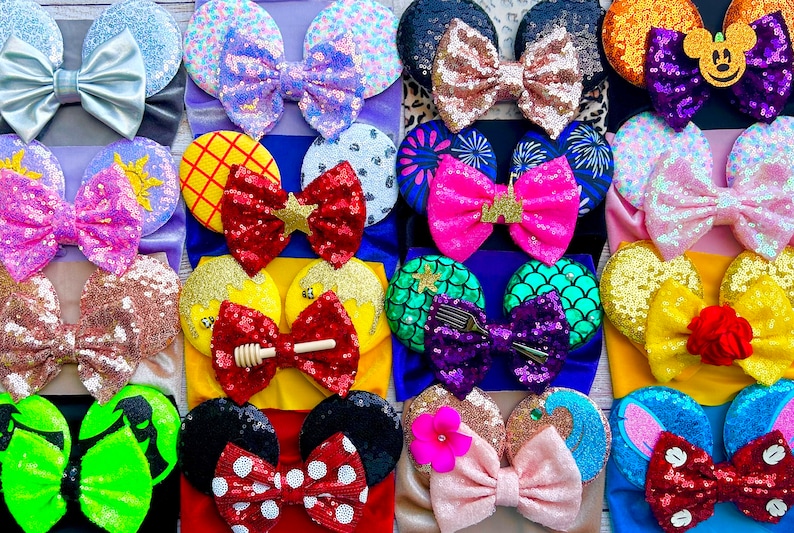 May include: A collection of 20 colorful Disney-themed hair bows with various characters and designs. The bows are made of sparkly sequins and feature a variety of colors, including pink, purple, blue, green, yellow, red, and orange.