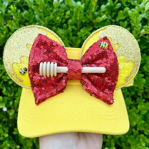 May include: Yellow sun hat with a red bow and a honey dipper. The hat has gold glitter ears with a bee design.