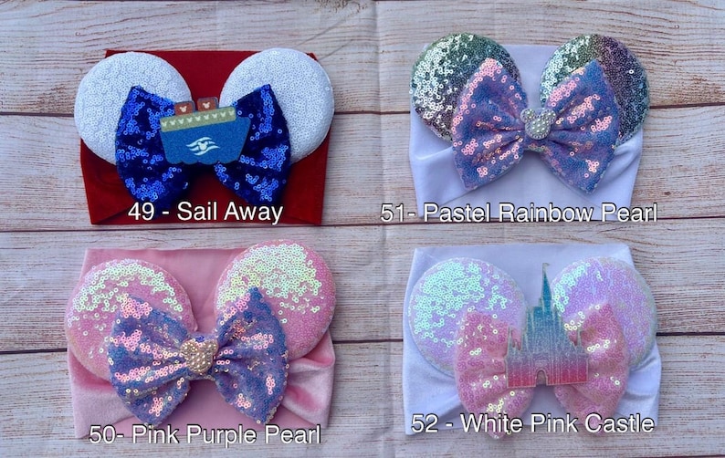 May include: Four different headband styles with various colors and designs. The headbands are made of soft fabric and feature a bow or ears. The designs include a blue and white ship, a rainbow with a pearl, a pink and purple bow with a pearl, and a white and pink castle.