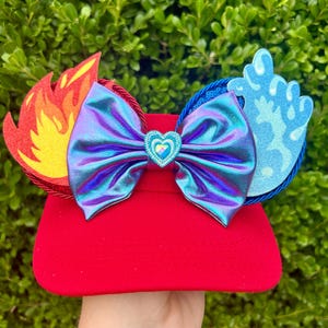 May include: Red, blue, and yellow fabric mouse ears with a large iridescent purple bow and a heart-shaped gem in the center. The ears are shaped like flames and water.