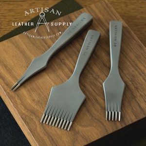 May include: Three matte grey metal leather stitching chisels with multiple prongs, each engraved with the text ARTISAN 3.0. The set includes one two-prong, one eight-prong, and one four-prong tool, all featuring a smooth, tapered handle design.