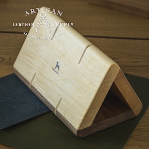 May include: A wooden box with a triangular shape, made of light and dark wood. The box is open and has a small, rectangular compartment inside. The box is labeled "Craft Leather" and has a logo of a compass with the text "Artisan Leather Supply".