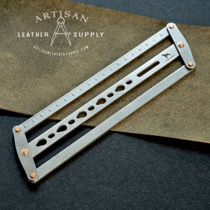 May include: A silver metal leather working tool with a ruler and various hole sizes. The tool is hinged and has copper-colored rivets. The text "ARTISAN LEATHER SUPPLY" and "ARTISANLEATHERSUPPLY.COM" are visible.