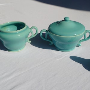 May include: A set of four teal ceramic kitchenware items, including a creamer, sugar bowl with lid, and two salt and pepper shakers.