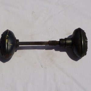 May include: A black metal door knob with a decorative design. The knob is attached to a metal rod.