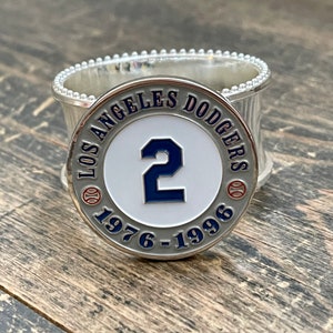 May include: A silver and blue Los Angeles Dodgers commemorative coin featuring the number "2" and the years "1976-1996".