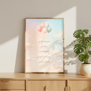 May include: A framed art print with a pastel sky background and a cluster of balloons. The print features handwritten text listing negative thoughts: perfectionism, grudges, overthinking, people-pleasing, and past mistakes. The frame is a light wood color.