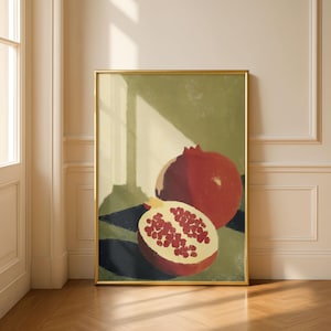 May include: A framed art print featuring a still life of pomegranates. One whole pomegranate and one cut in half, revealing the seeds. The background is a mix of green, black, and beige tones, with a gold frame.