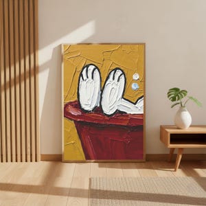 May include: Oil painting of cartoon feet in a red bathtub against a yellow background. The artwork is framed in a wooden frame. The painting has a textured, impasto style, with visible brushstrokes. The artwork is displayed in a room with wooden floors and a side table.