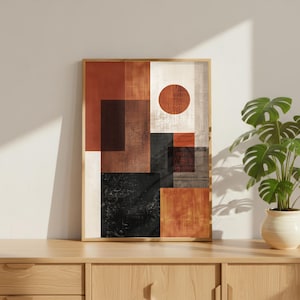 May include: Abstract art print in a wooden frame. The artwork features a geometric design with squares, rectangles, and a circle in shades of brown, black, and white. The print is displayed on a wooden cabinet with a potted plant.