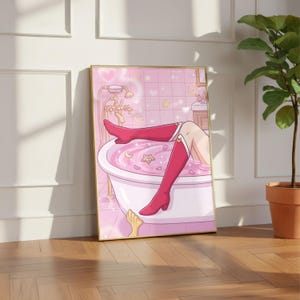 May include: A framed print showing an anime-style illustration of a person in a pink bathtub, wearing red boots. The bathroom has pink tiles and gold fixtures. The print is displayed on a wooden floor.