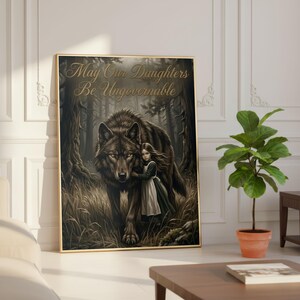 May include: A framed art print featuring a girl embracing a large wolf in a forest setting. The artwork is in muted tones with the text "May Our Daughters Be Ungovernable" in gold script across the top. The print is displayed in a gold frame.