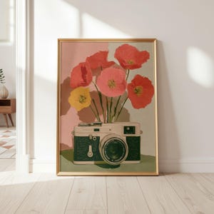 May include: A framed art print featuring a vintage camera with a bouquet of red, pink, and yellow flowers. The camera is two-toned, with a black base and a cream-colored top. The background is split between pink and light gray.