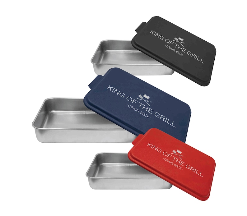 May include: Three silver baking pans with matching lids. The lids are black, navy blue, and red. Each lid has the text "King of the Grill - Craig Beck." printed in white.