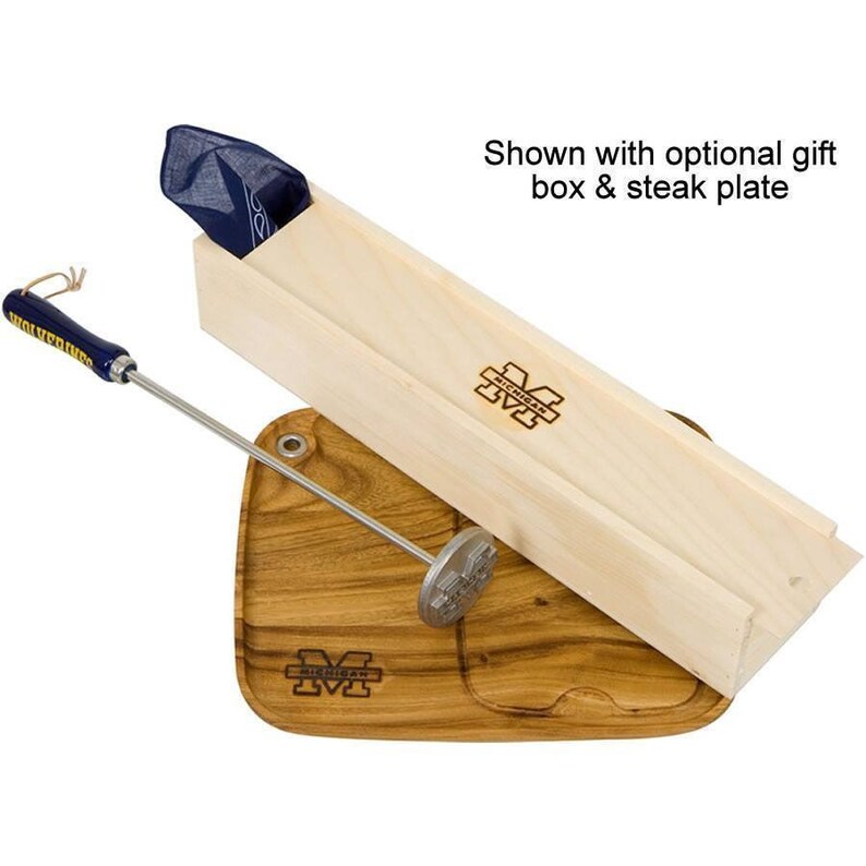 May include: A wooden box with a blue bandana inside, a wooden chopping board with a metal steak branding iron, and a wooden handle with a metal rod. The box and chopping board are both engraved with the University of Michigan logo.