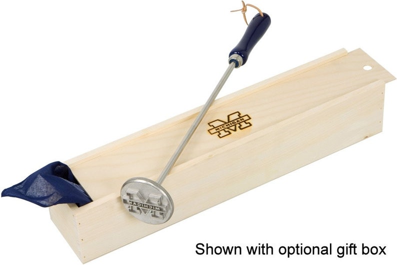 May include: A silver metal branding iron with a blue wooden handle and the University of Michigan logo. The branding iron is in a wooden box with the University of Michigan logo.