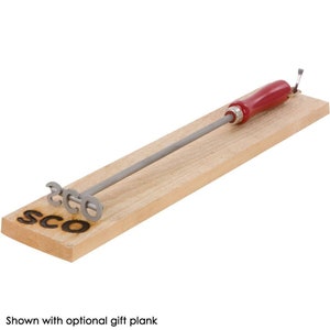 May include: A metal skewer with a red wooden handle and a wooden base with the word "SCO" burned into it. The skewer is designed to hold a hot dog or sausage while it is being cooked over a fire.
