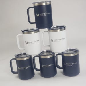 May include: A stack of insulated travel mugs in navy blue and white. Each mug has a silver rim, a handle, and a clear lid. The Worthington Industries logo is printed on the side of each mug.