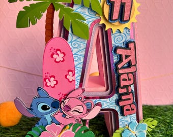 May include: A pink and blue 3D letter A cake topper with a palm tree, surfboard, sun, and Stitch and Angel characters. The letter A is decorated with a blue and white wave pattern. The sun has the number 11 in the center. The cake topper says "Aleina" on the side.