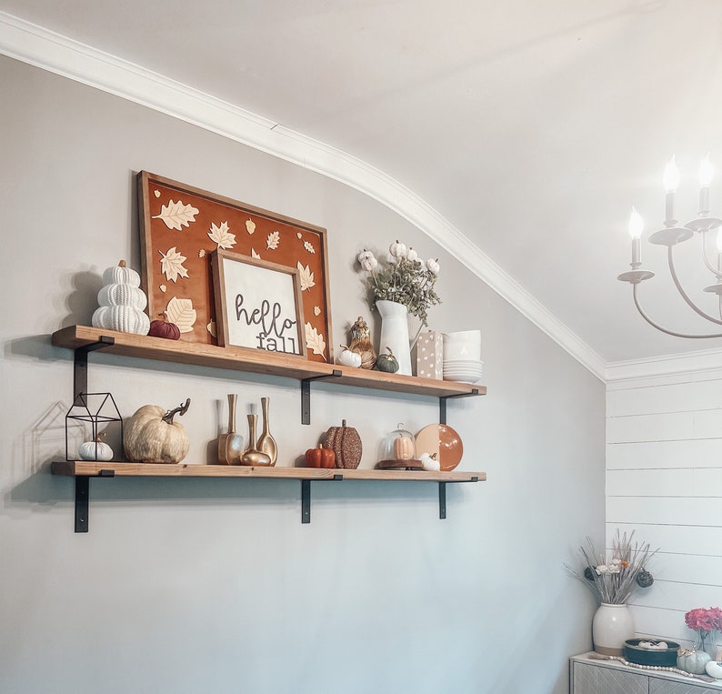 May include: Two wooden shelves with black metal brackets, decorated with fall-themed items, including pumpkins, gourds, leaves, and a sign that says "hello fall".
